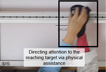 A person engaged in a rehabilitation game. The person reaches from out of frame toward a target. There is text on top of the image that says: Directing attention to the reaching target via physical assistance.